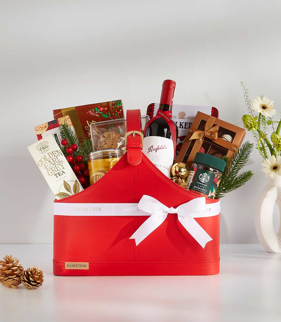 Red faux leather wine gift basket with red wine, tea, cookies, chocolates, honey, and festive holiday accents including gold