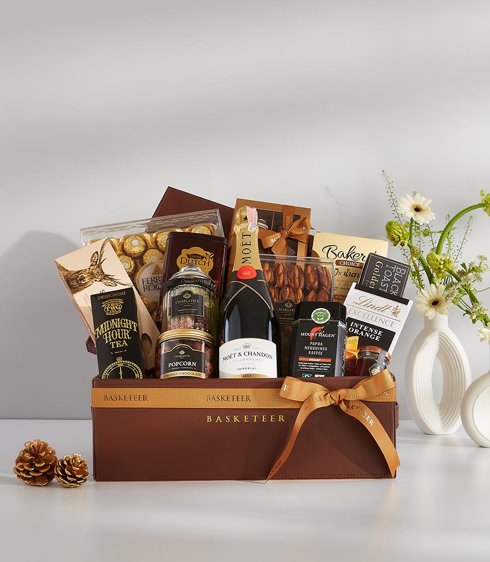 Luxury champagne and gourmet gift basket with chocolates, tea, and artisan snacks in dark brown leather box