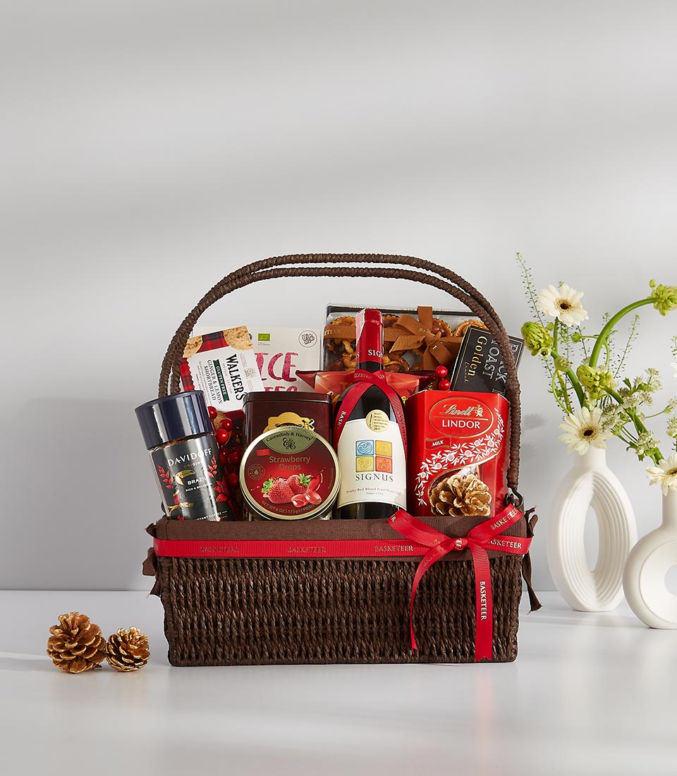 Dark brown woven gift basket with red wine, gourmet coffee, chocolates, shortbread, and artisan goods with white daisies