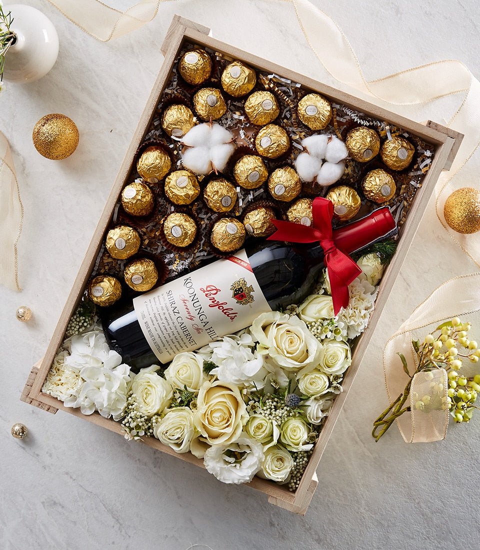 Luxury wine and flower gift box with red Shiraz, white roses, hydrangeas, and gold chocolates in wooden presentation