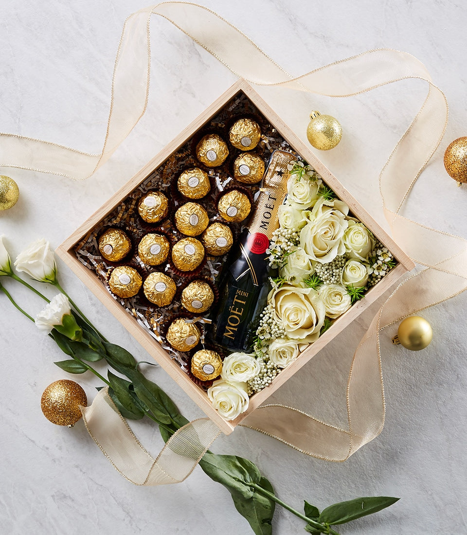 Luxury champagne gift box with gold-wrapped chocolates, white roses, and sparkling wine on marble