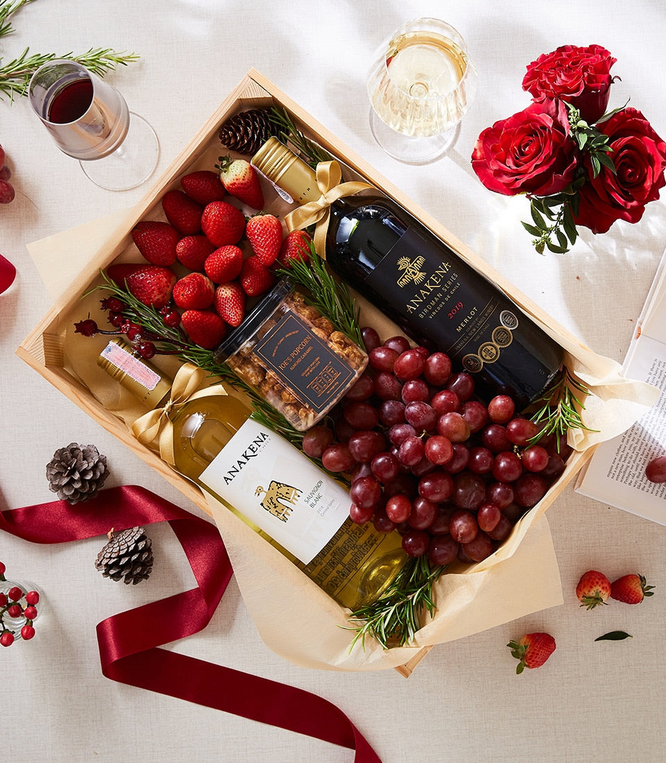 Luxury wine gift box with red and white bottles, fresh strawberries, grapes, popcorn, and rosemary sprigs
