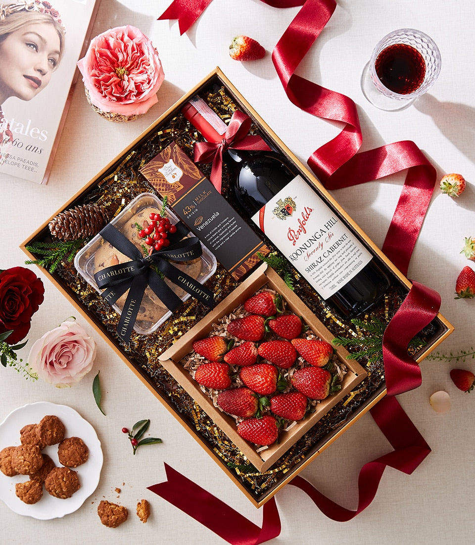 Luxury red wine gift box with dark chocolate, fresh strawberries, and gourmet cookies tied with red ribbon