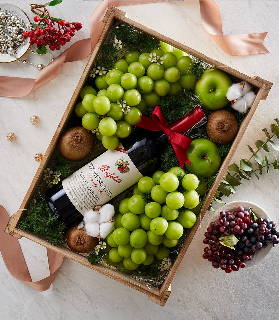 Premium wooden crate with red wine, green grapes, fresh fruit, and natural foliage styling