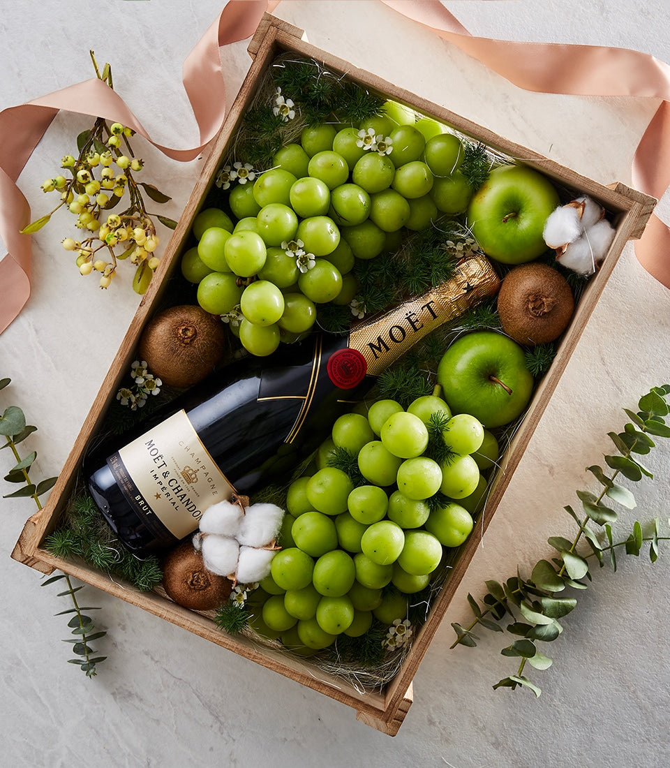 Moët & Chandon champagne gift box with green grapes, apples, kiwis, and fresh florals in rustic wooden crate