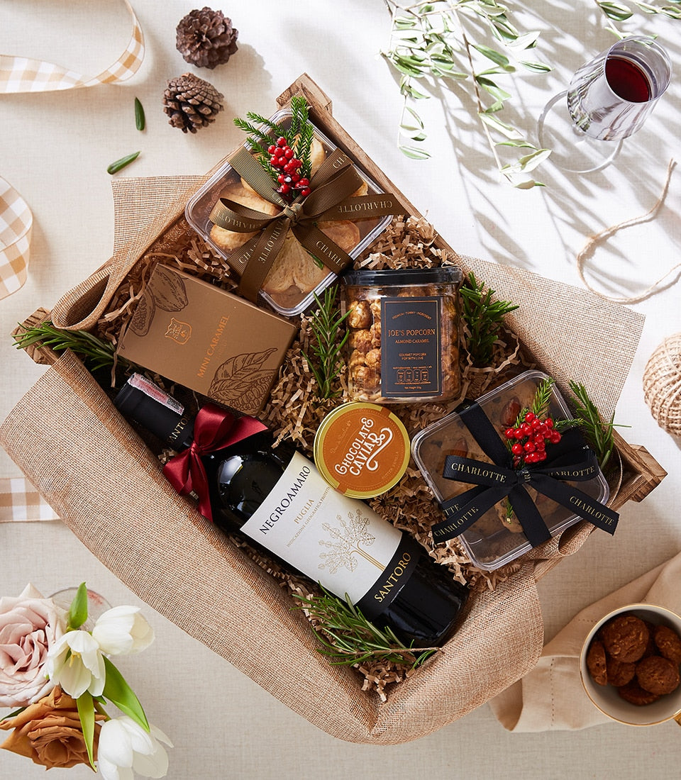 Luxury wine and chocolate gift basket with red wine, artisan caramel, popcorn, and baked goods in woven hamper
