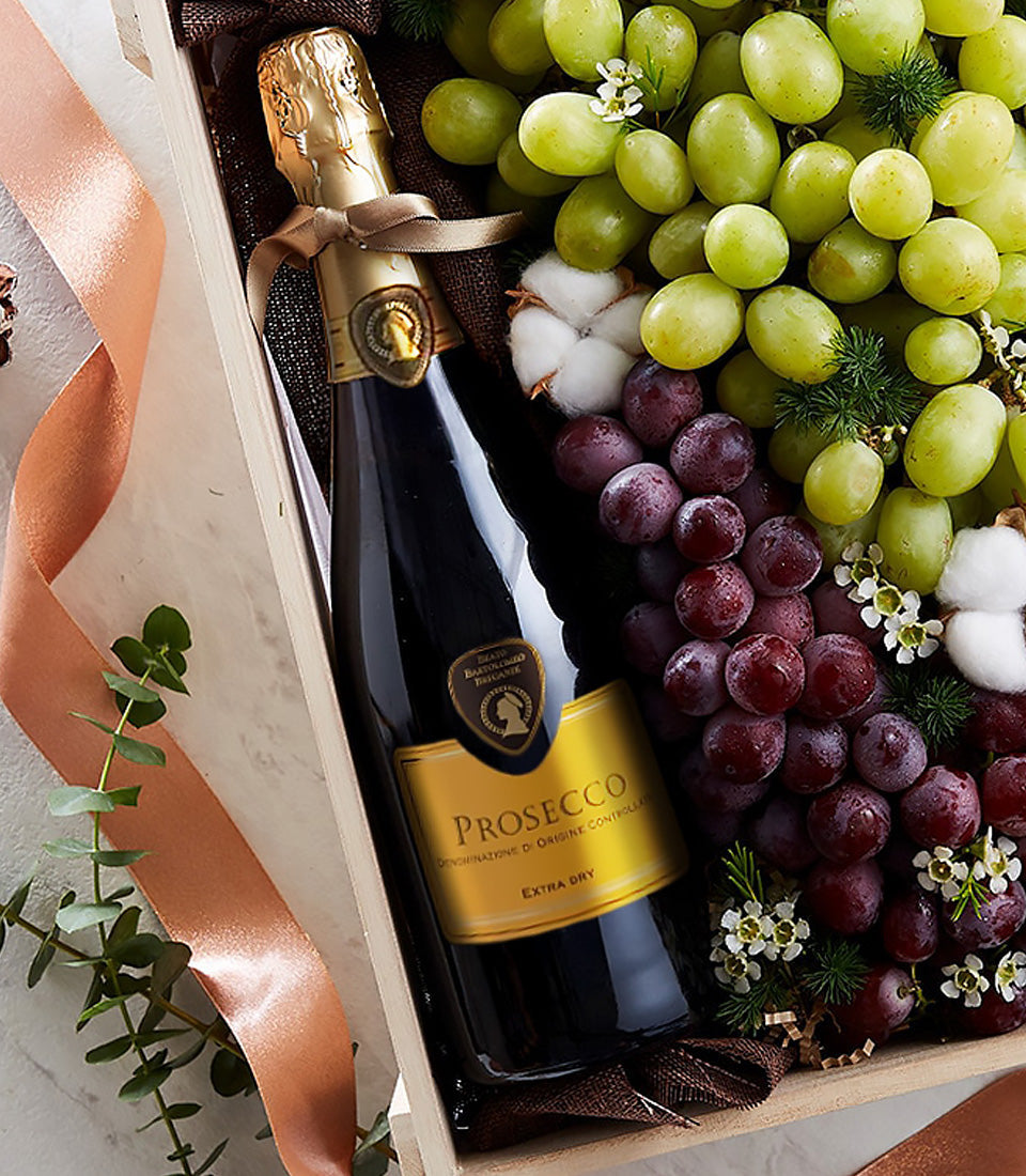 Prosecco sparkling wine gift box with fresh green and red grapes, white flowers, and peach satin ribbon