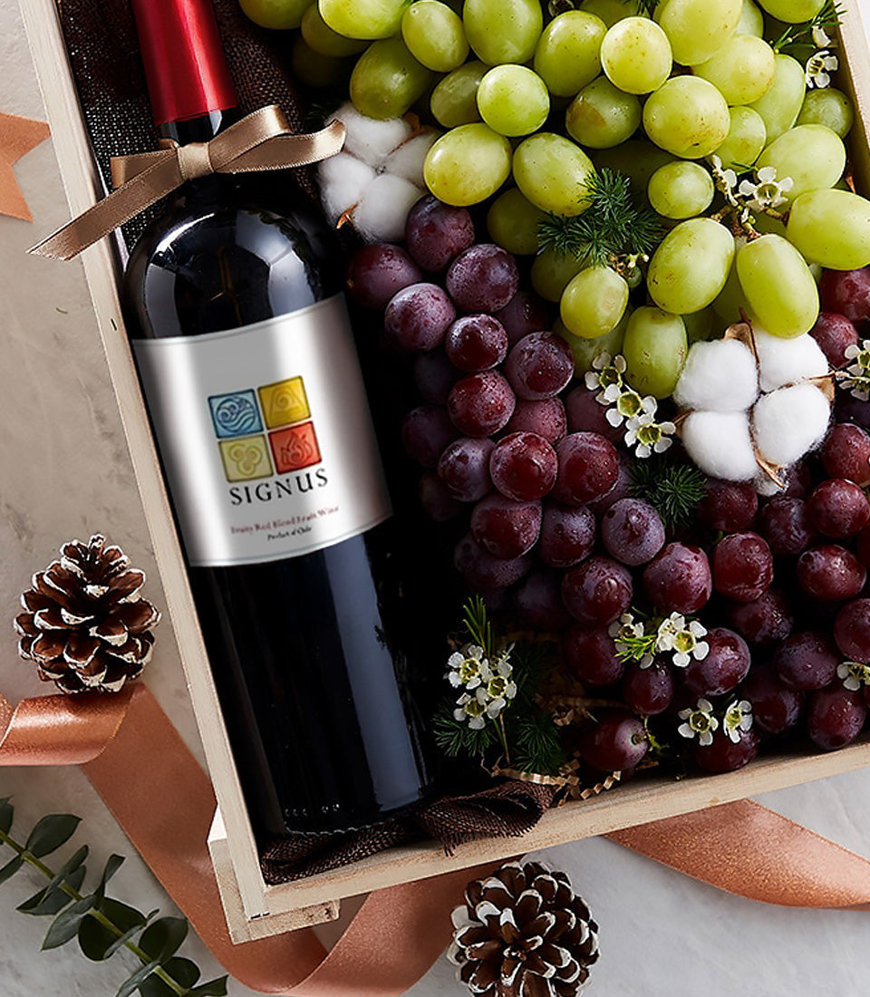 Luxury red wine bottle with fresh grapes in wooden gift box, topped with copper ribbon and natural flourishes
