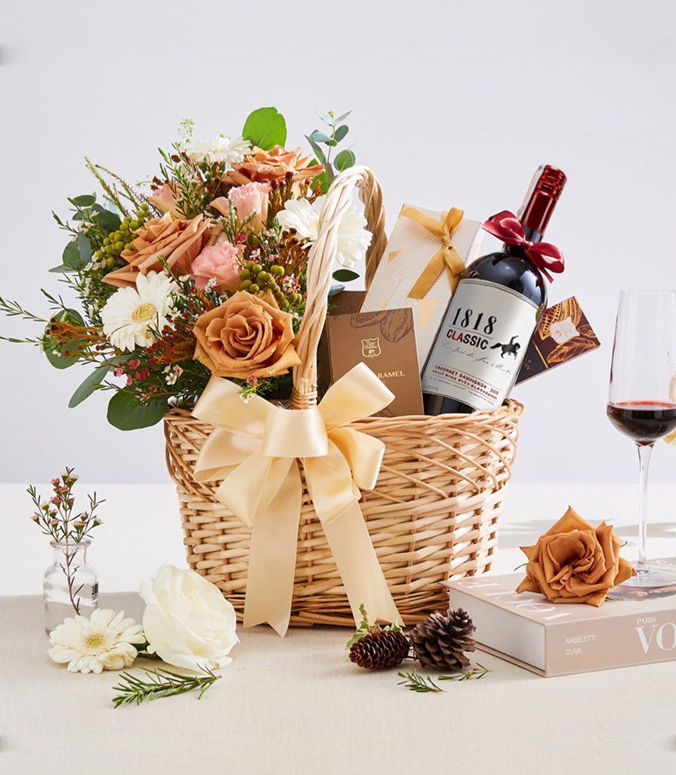 Luxury gift basket with red wine, fresh flowers, and gourmet treats in woven wicker with gold ribbon bow