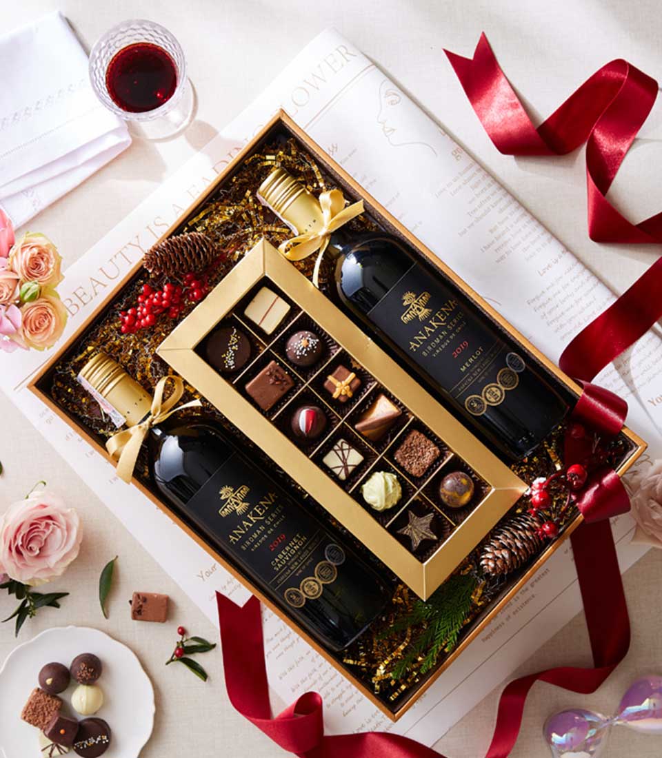 Luxury gift box with two red wines, assorted chocolates, and gold ribbon presentation for wine lovers
