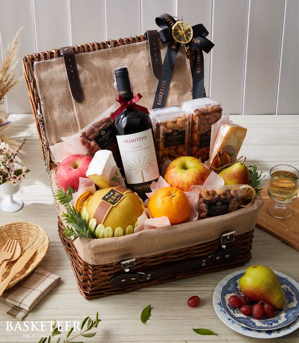 Wicker picnic basket with red wine, artisan cheese, fresh fruit, and roasted nuts for gourmet gifting