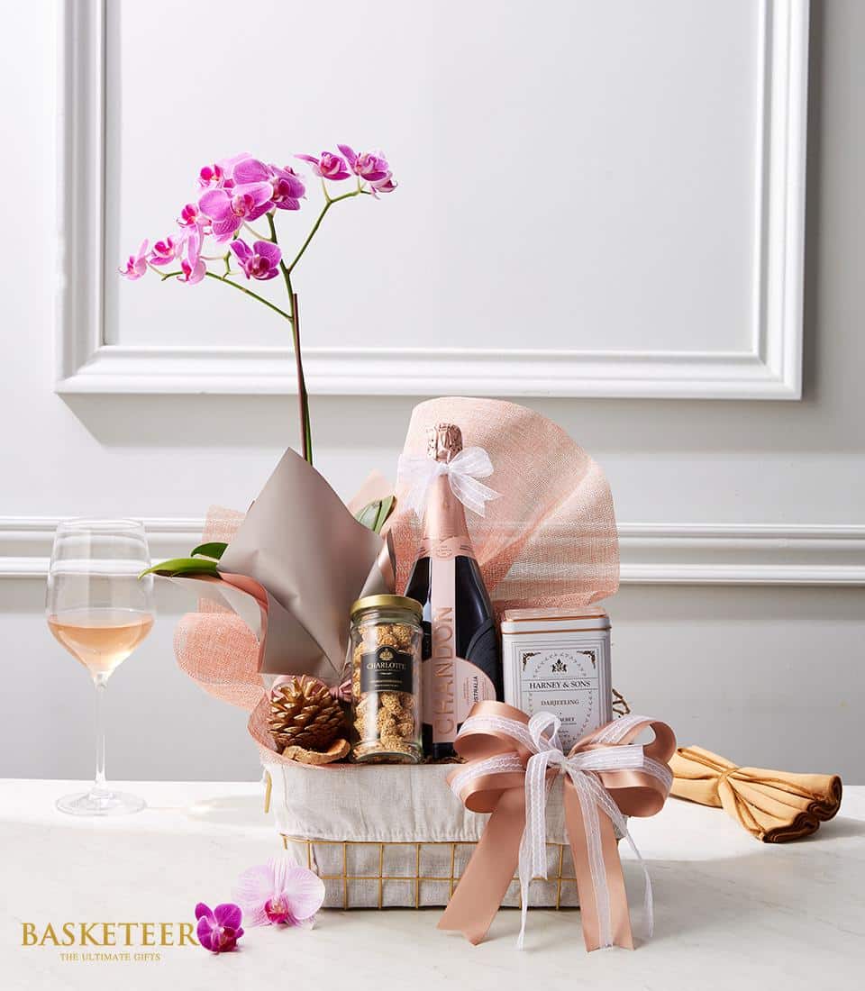 Luxury gift basket with Rosé champagne, pink orchid plant, gourmet cookies, and Darjeeling tea in white woven basket with