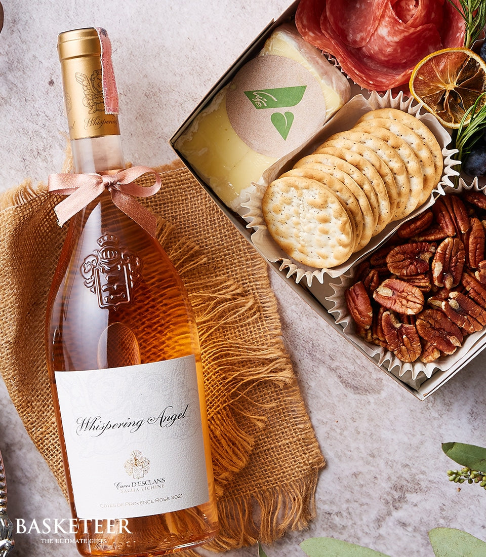 Rosé wine with gold foil and pink ribbon paired with artisan charcuterie, cheese, crackers, and pecans in luxury gift set