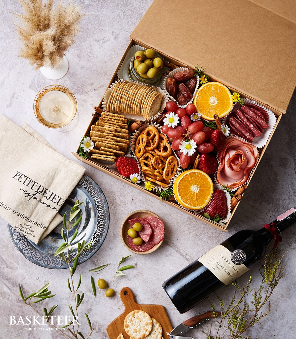 Luxury charcuterie and wine gift box with gourmet meats, artisan crackers, fresh fruits, and red wine
