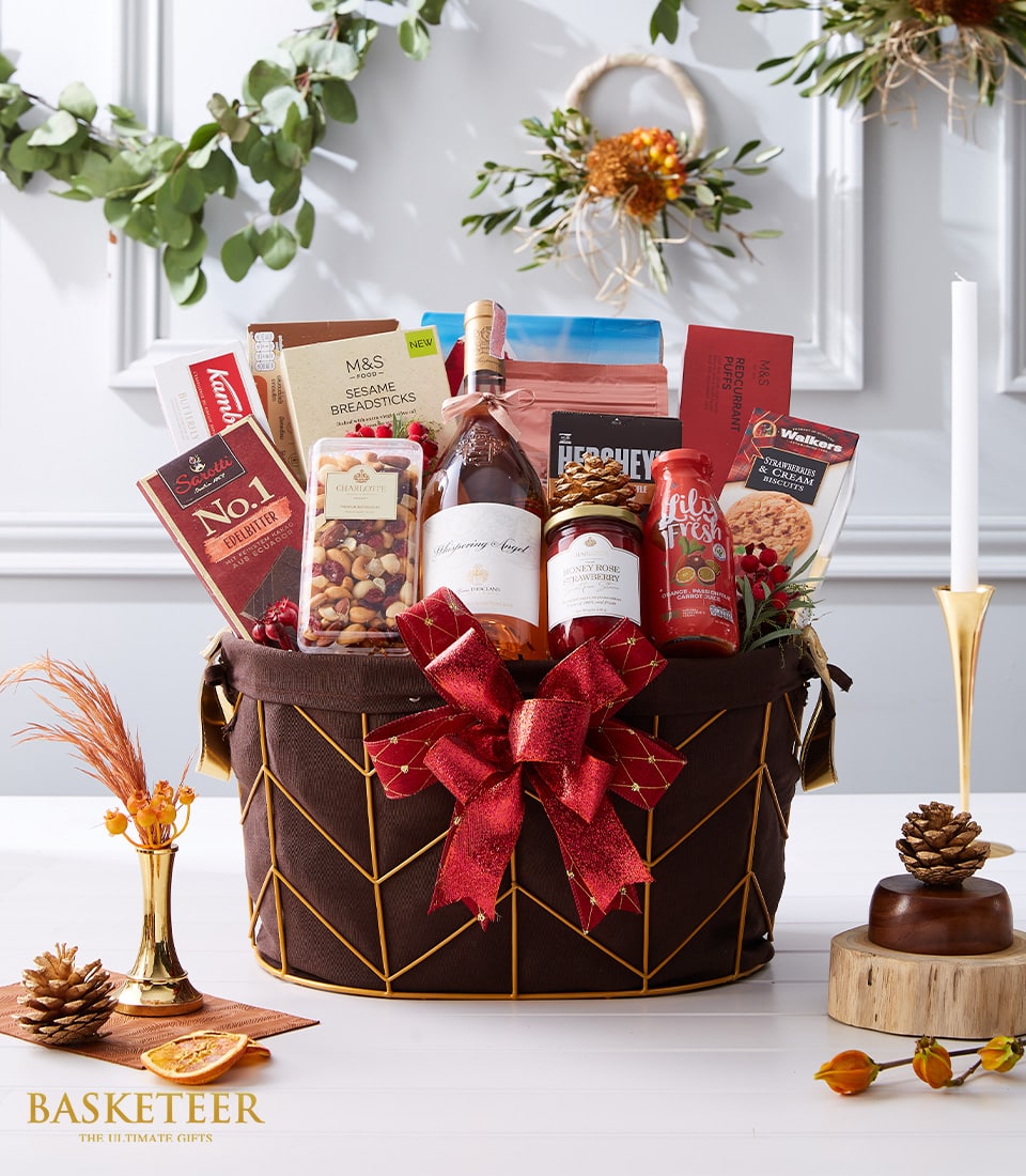 Luxury rosé wine gift hamper with gourmet chocolate, jam, biscuits, and nuts in dark fabric basket with gold wire frame
