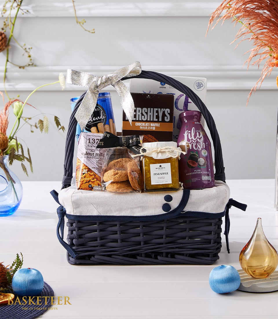 Dark grey woven gift basket filled with chocolate waffle, pineapple spread, mangosteen juice, and gourmet treats, tied with