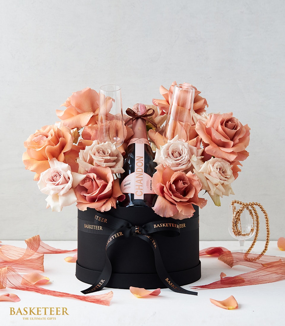 Luxury sparkling wine gift box with fresh peach and coral roses, Chandon bottle, champagne flutes, and black hatbox with
