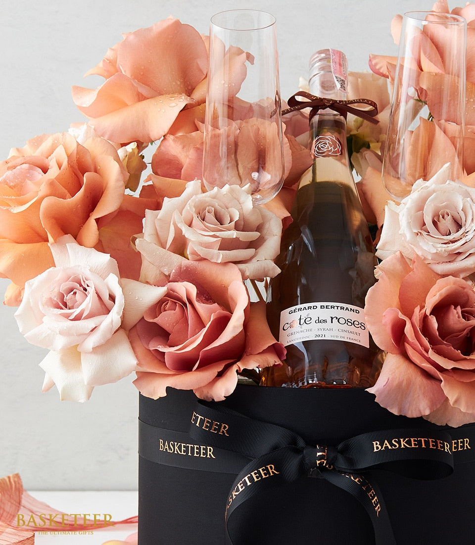 Luxe rosé wine gift set with fresh peach and blush roses, champagne flutes, and black presentation box