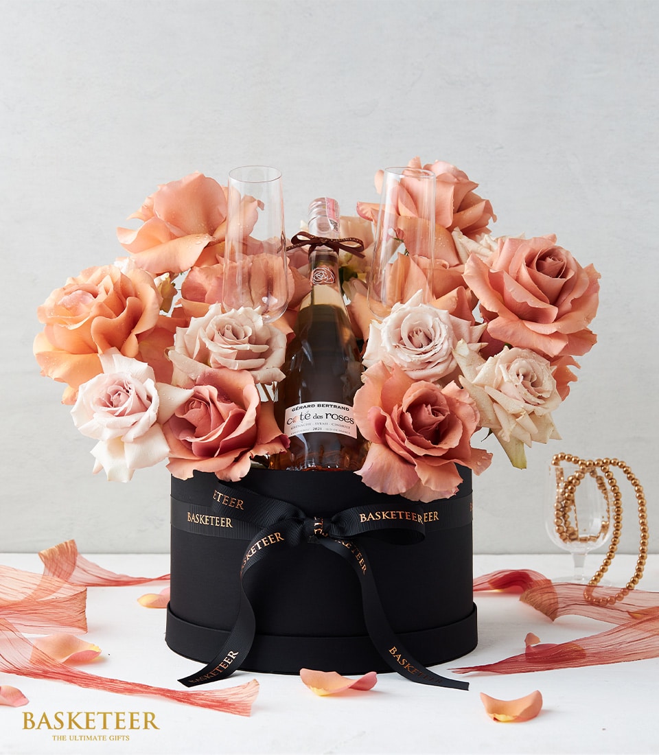 Luxury rosé wine gift box with peach and blush roses, champagne flutes, and black hatbox for anniversary celebrations
