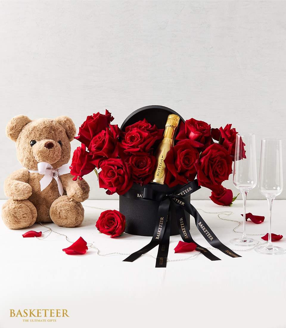 Romantic anniversary gift set with red roses, teddy bear, and sparkling wine in luxury hatbox