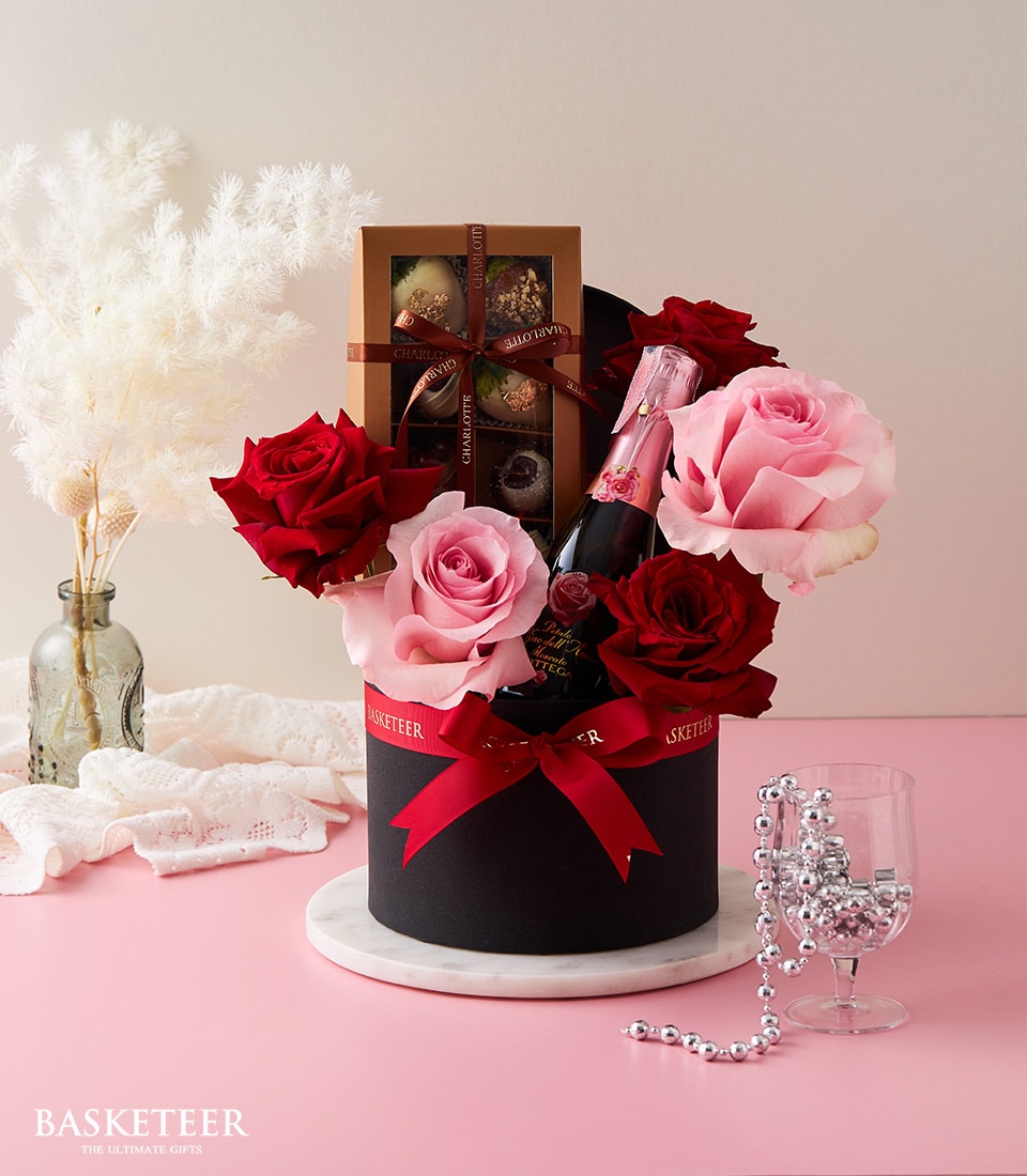 Luxury gift box with pink sparkling wine, red and pink roses, artisan chocolates, and crystal glassware for anniversary
