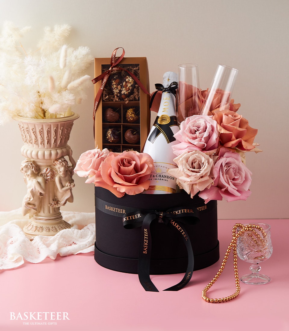 Moët & Chandon champagne with peach and blush roses, chocolate-covered apples, and champagne flutes in luxury black hatbox