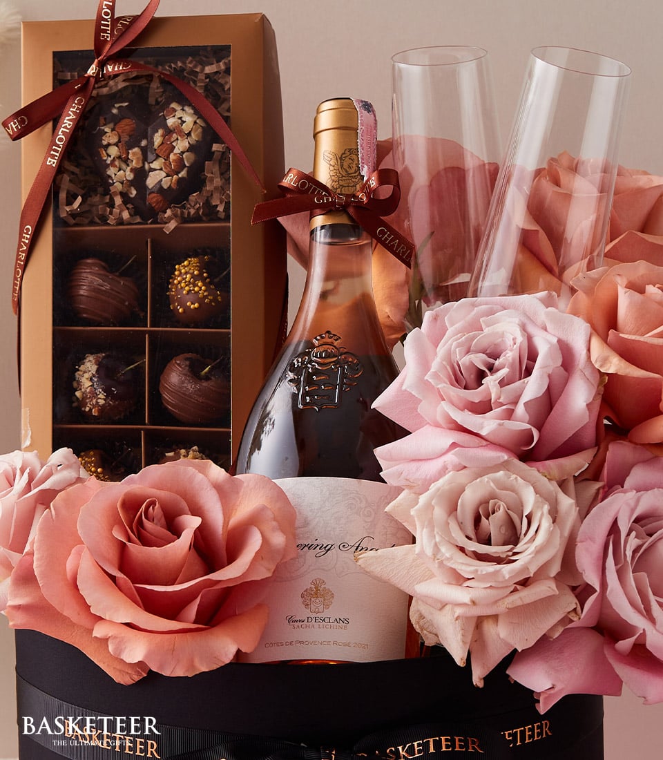 Rosé wine, fresh pink roses, artisan chocolates and champagne flutes in luxury anniversary gift box