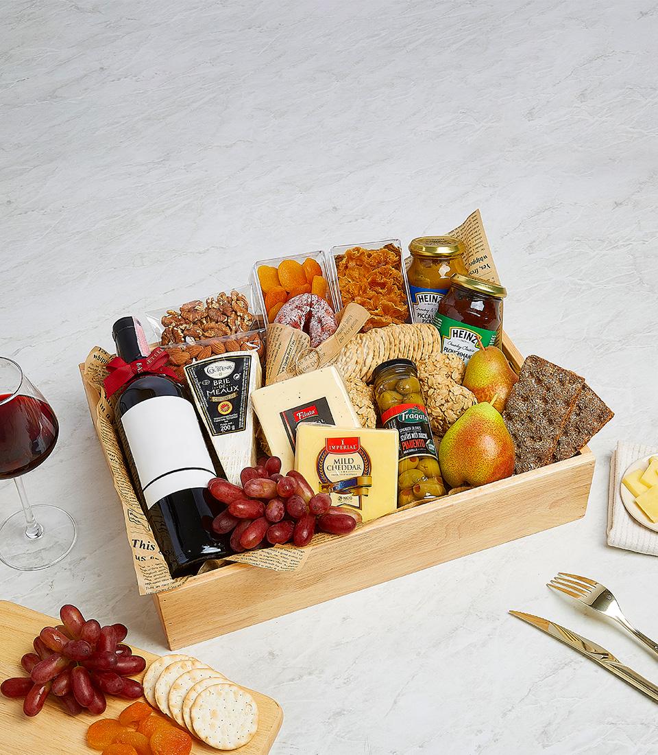 Premium red wine and gourmet cheese gift basket with crackers, preserves, and dried fruits in wooden tray