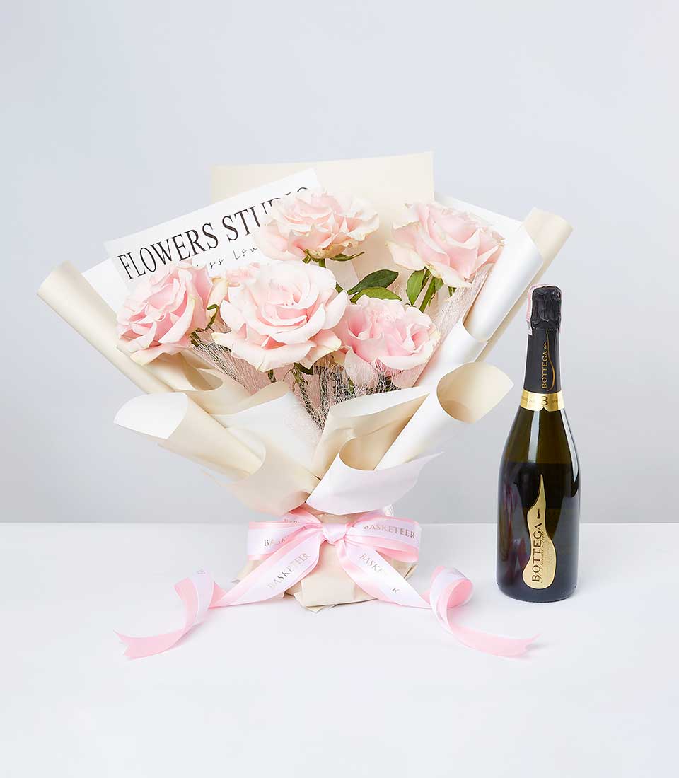 Light pink roses with sparkling wine bottle, cream paper wrap, and pink Basketeer ribbon bow
