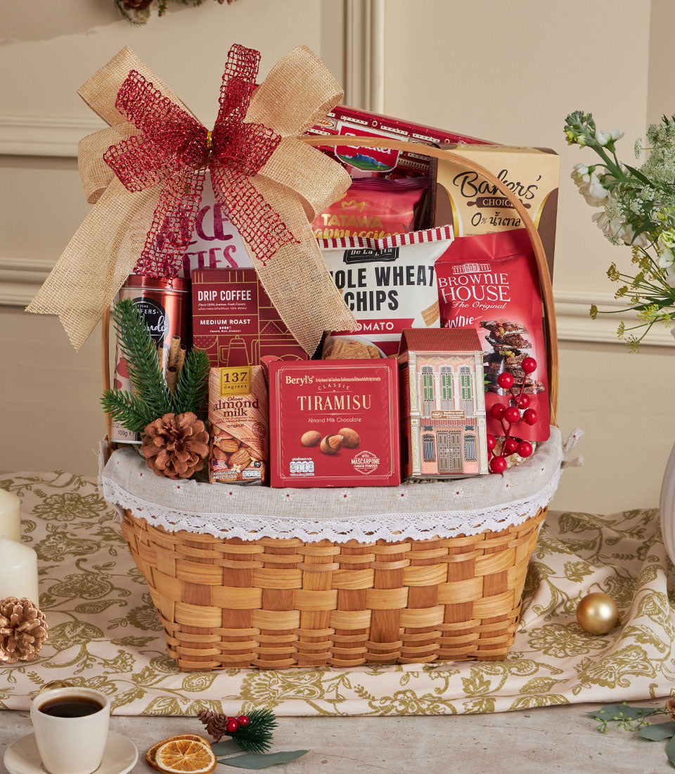 Woven wicker gift basket with premium drip coffee, chocolate, almond milk, and gourmet snacks tied with red burlap ribbon