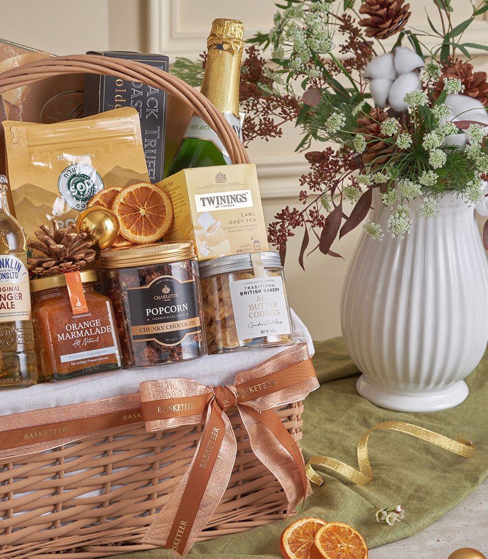 Golden wicker gourmet basket with sparkling wine, Earl Grey tea, marmalade, and artisan treats tied with copper ribbon for