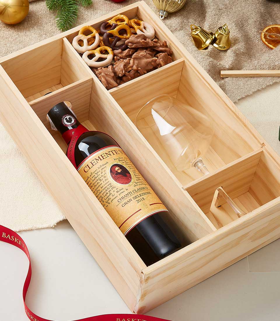 Wooden gift box with red wine bottle, wine glass, chocolate-covered pretzels, and nut clusters for holiday gifting