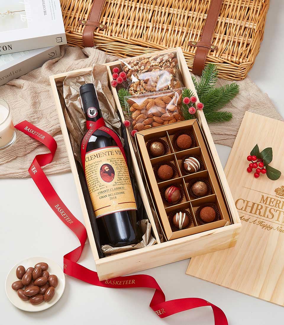 Chianti Classico red wine with chocolate truffles, nuts, and evergreen in wooden gift box with red ribbon