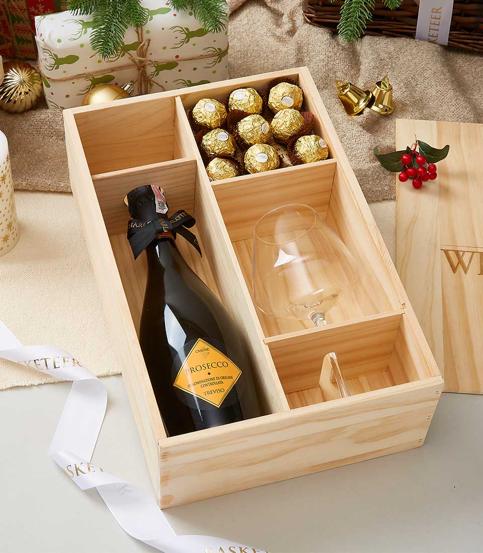 Premium Prosecco, gold-foiled chocolates and wine glass in wooden gift box with festive red berry sprig