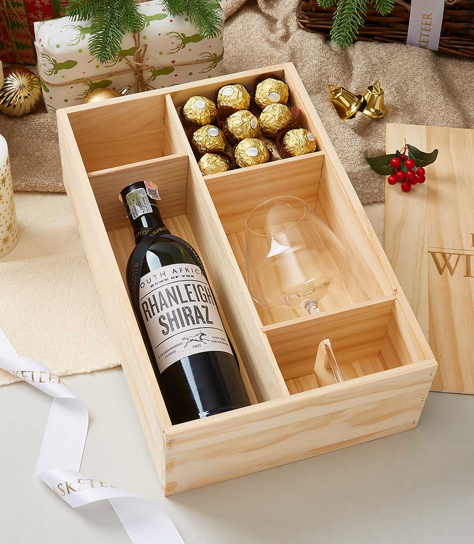 Wooden gift box with red wine, wine glass, and gold-wrapped chocolates, festive holiday presentation