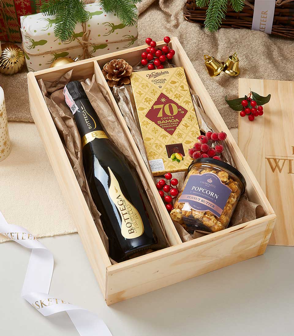 Premium sparkling wine and gold-wrapped chocolate in festive wooden crate with holiday berries and popcorn