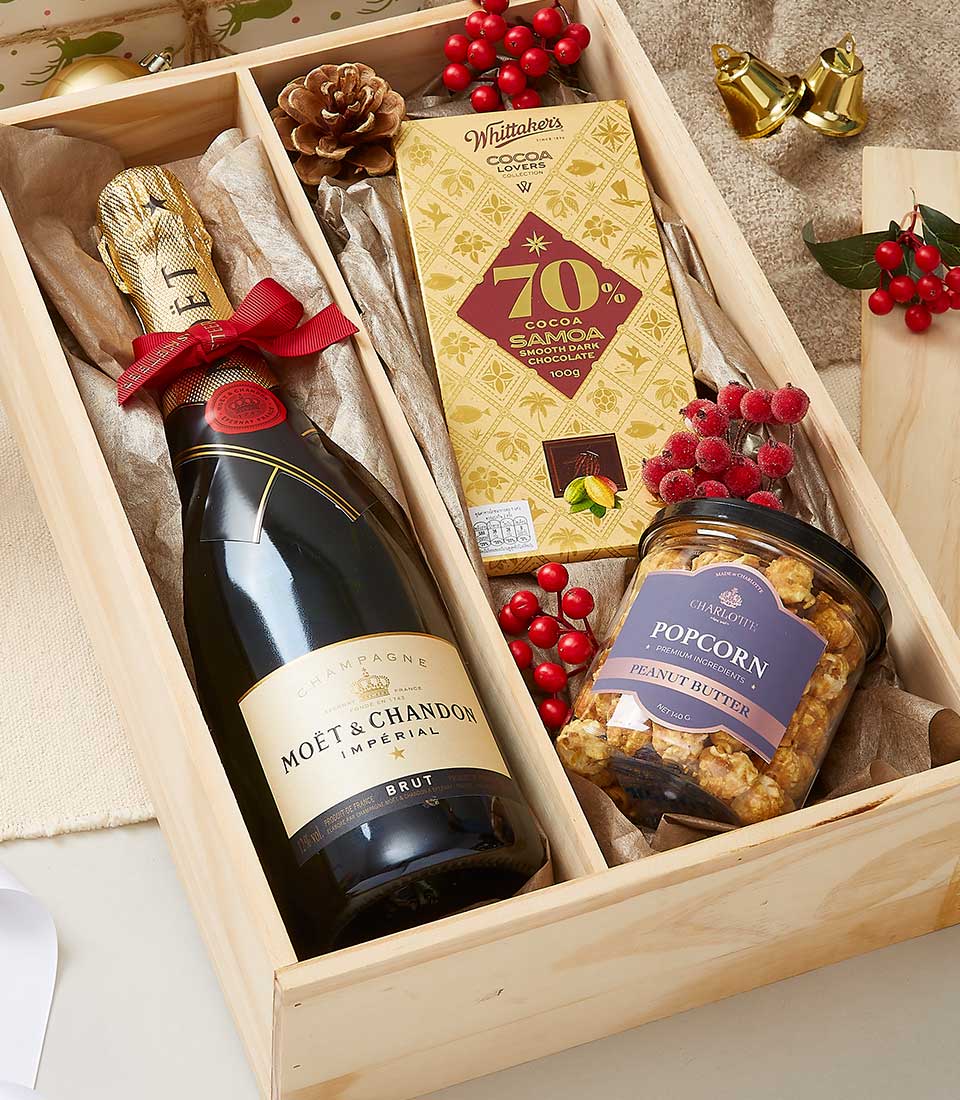 Champagne, artisan chocolate, and popcorn gift box with festive red berries and golden accents