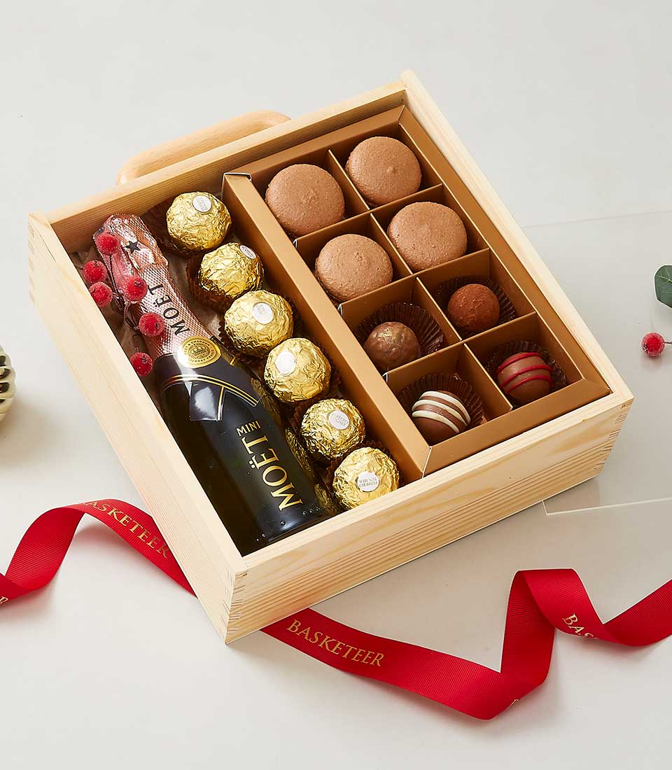 Luxury wooden gift box with champagne, gold-foiled chocolates, macarons, and truffles tied with red ribbon
