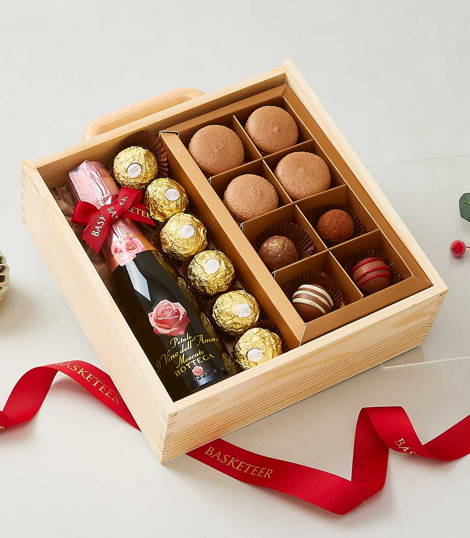 Wooden gift box with sparkling wine, gold-foiled chocolates, macarons, and luxury truffles