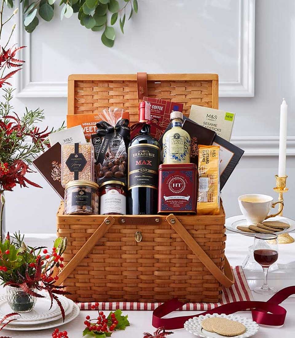 Woven wicker luxury picnic basket filled with red wine, gourmet treats, and artisan goods on festive white tablecloth