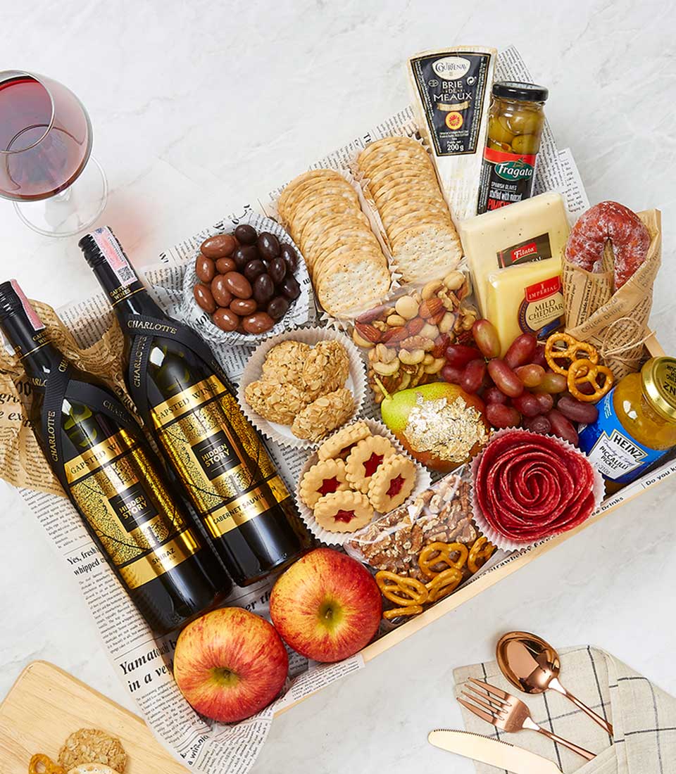 Luxury wine and gourmet gift hamper with red wines, artisan cheeses, cured meats, fresh fruit, and gourmet treats in wooden