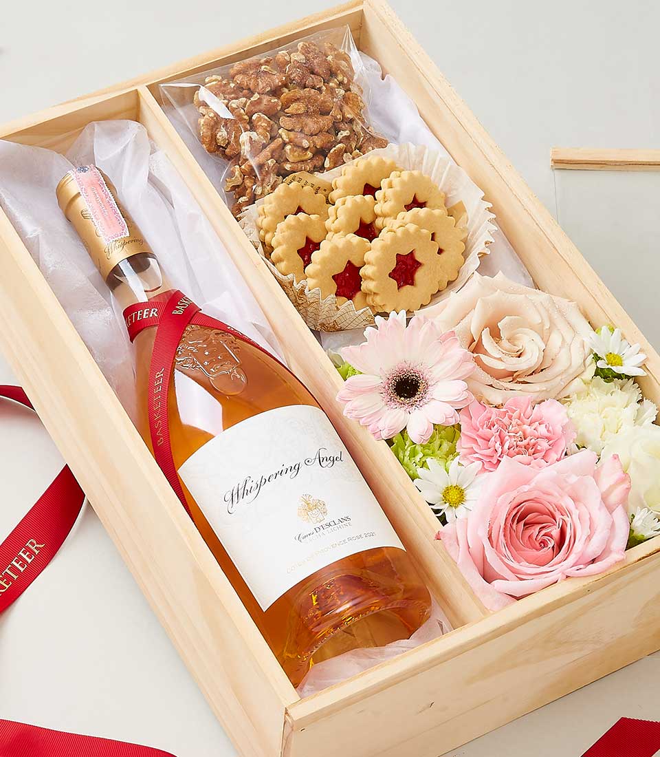 Rosé wine, star cookies, walnuts, and fresh pink roses in wooden gift box with red ribbon