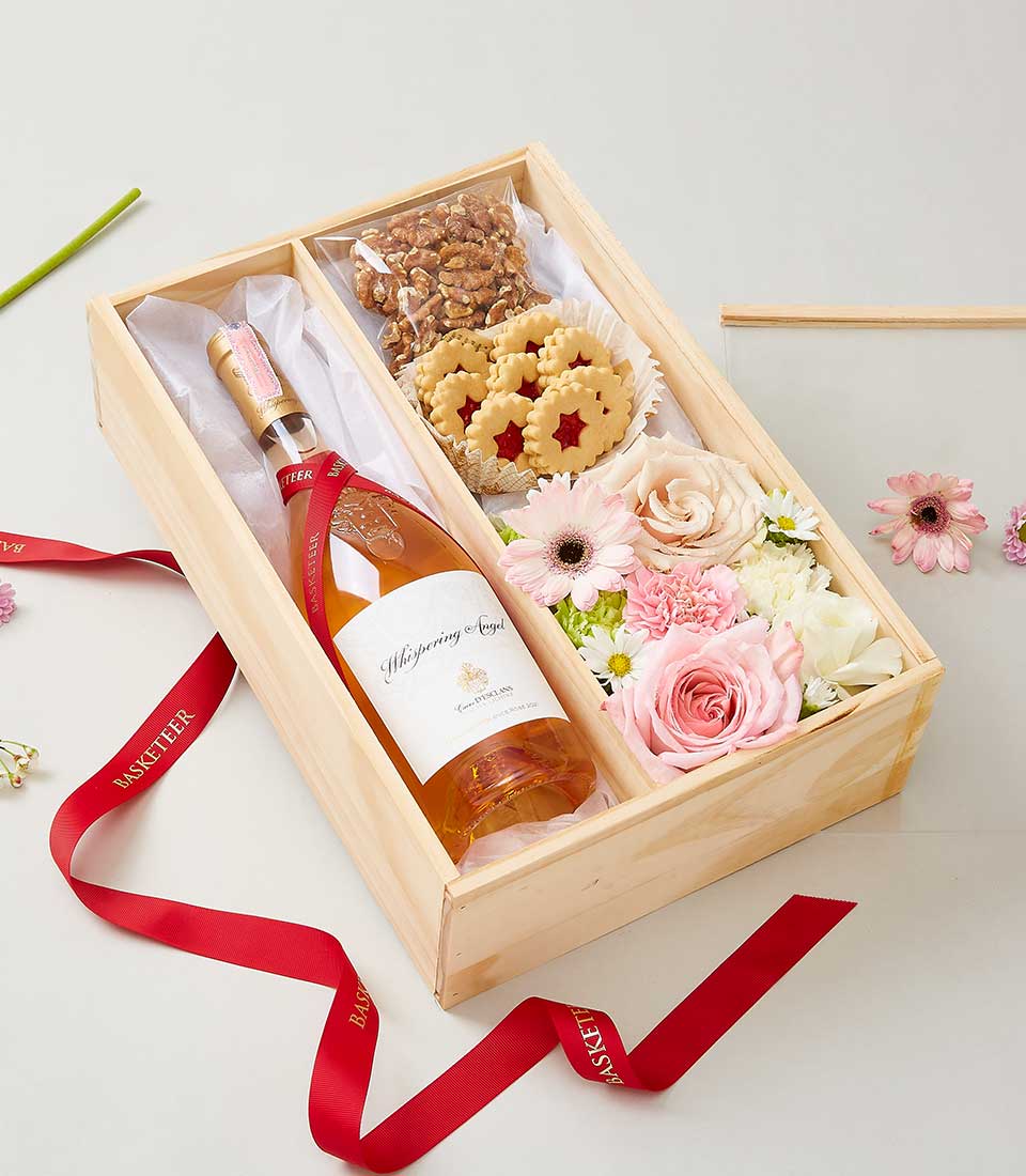 Rosé wine, cookies, walnuts and fresh pink roses in wooden gift box with red ribbon