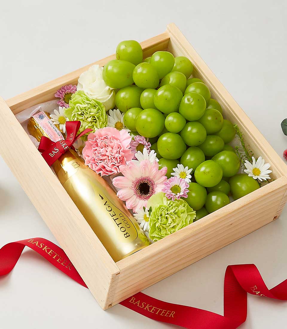 Premium sparkling wine with fresh roses, carnations, and green grapes in wooden gift box