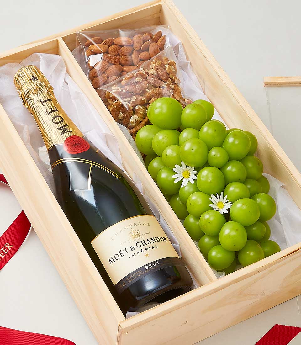Moët & Chandon champagne gift box with almonds, walnuts, and green grapes on white tissue, elegant wooden presentation