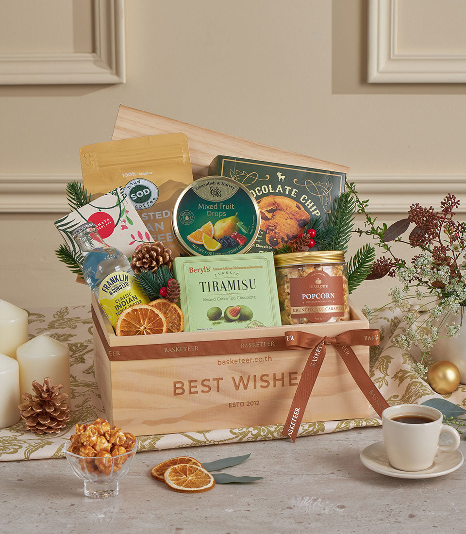 Wooden gift basket with gourmet coffee, tonic water, chocolates, and festive treats, tied with brown ribbon for New Year