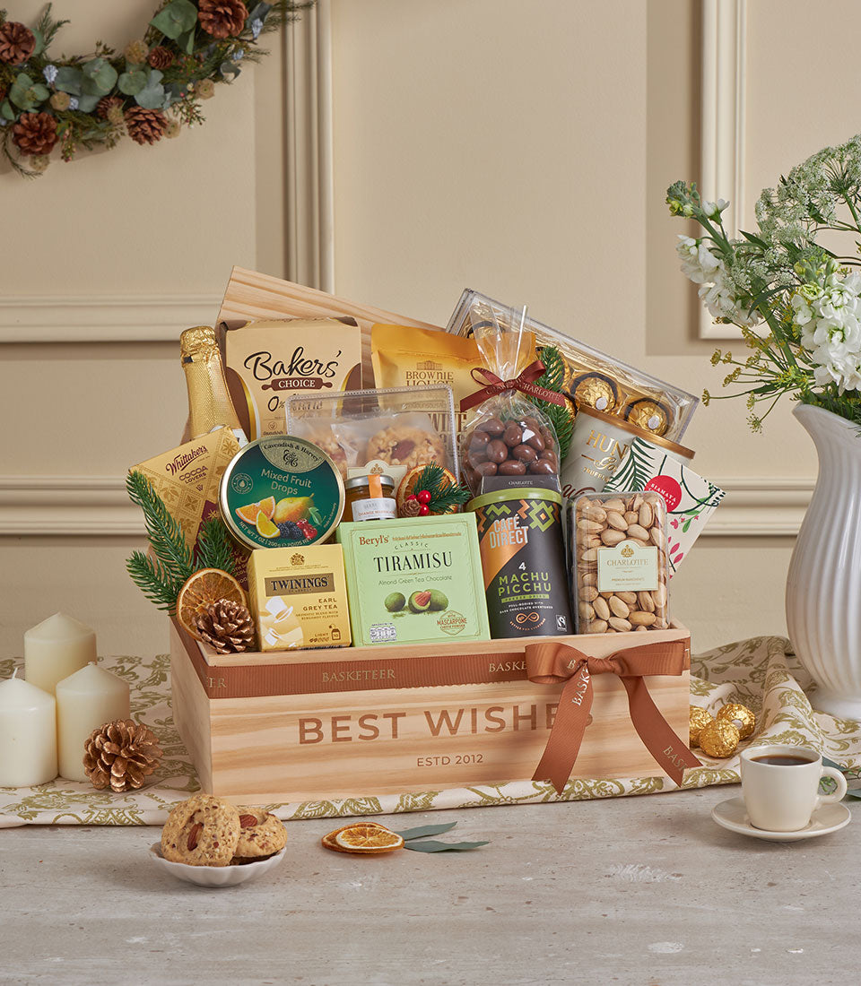 Golden deluxe gourmet gift hamper in wooden crate with champagne, chocolates, jam, coffee, and festive greenery for New Year