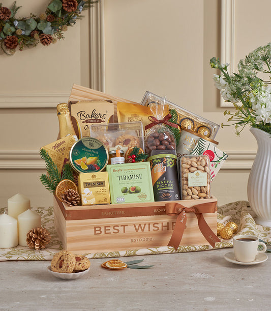 Golden deluxe gourmet gift hamper in wooden crate with champagne, chocolates, jam, coffee, and festive greenery for New Year