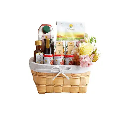Light brown woven wicker basket with white linen liner, filled with gourmet treats and fresh yellow roses and pink hydrangeas