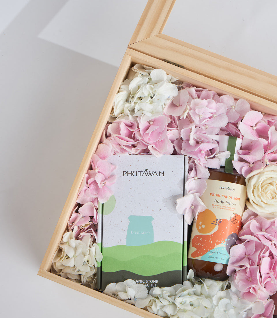 Luxury spa gift set in wooden box with pink and white hydrangeas, ceramic stone sachet, body lotion, and botanical products from Phutawan brand.